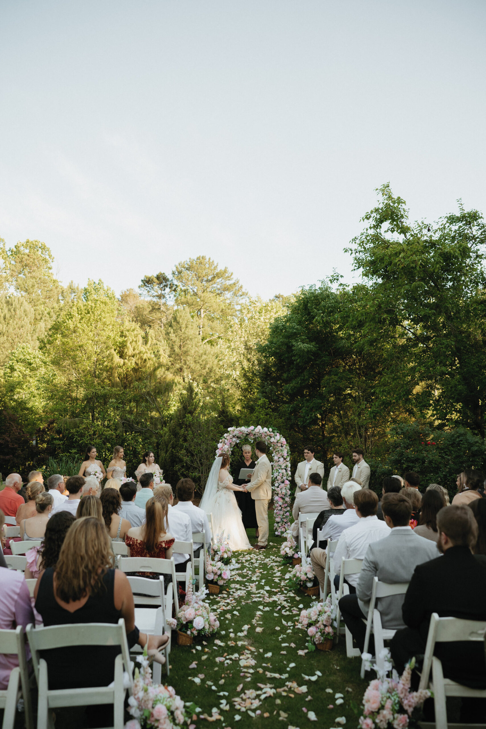 Guests gathered for an outdoor wedding ceremony with a flower-lined aisle and full wedding party.